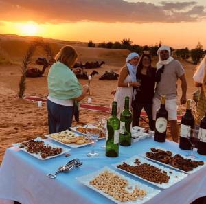 a group of people standing around a table with food and wine at Mourad desert camp in Merzouga