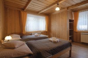 two beds in a room with wooden walls and windows at Gościniec u Marzeny in Bukowina Tatrzańska