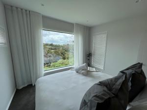 a bedroom with a bed and a large window at Hidden Valley Waiheke in Palm Beach