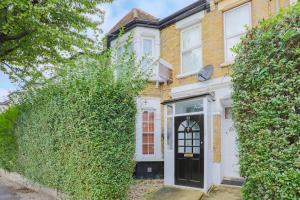 a white house with a black door and ivy at 2 Bed Garden Flat Leyton Village in London