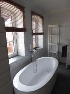 La salle de bains est pourvue d'une baignoire blanche et de 2 fenêtres. dans l'établissement Ferienwohnung Elise im Gulfhof am Kanal, à Großefehn 