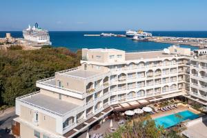 a large white building with a swimming pool next to the ocean at Athineon Hotel in Rhodes Town
