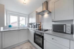 a kitchen with white cabinets and a sink and a microwave at Sea Breeze Apartment in Walton-on-the-Naze