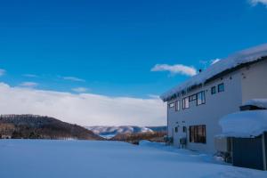 ein schneebedecktes Gebäude mit Bergen im Hintergrund in der Unterkunft 山の源-Yama No Minamoto in Furano