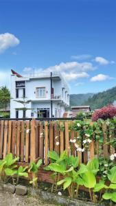 a white house behind a wooden fence with flowers at Depik Inn in Takengon