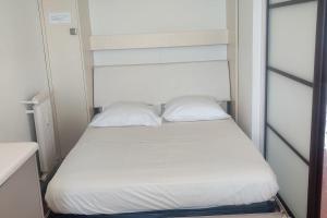 uma cama num pequeno quarto com lençóis brancos e almofadas em Bel appartement climatisé vue mer parking gratuit. em Villefranche-sur-Mer