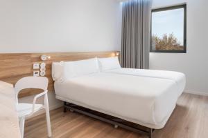 a bedroom with a white bed and a chair at B&B HOTEL Lisboa Oeiras in Oeiras