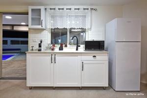 cocina con armarios blancos y nevera blanca en שרדונה - סוויטה מהממת עם ג'קוזי ובריכה פרטית מחוממת ומקורה, en ‘Ein Ya‘aqov