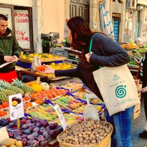 a woman standing in front of a fruit market at Hotel Posta in Siracusa
