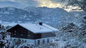 a house covered in snow with mountains in the background at Ferienwohnung Panoramablick in Bolsterlang
