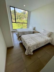 - 2 lits dans une chambre avec une grande fenêtre dans l'établissement Cómodo Apartamento en Manizales, à Manizales