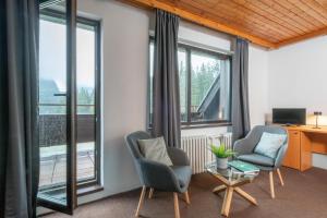 a living room with two chairs and a table and windows at Wellness Hotel Šedý Vlk in Harrachov