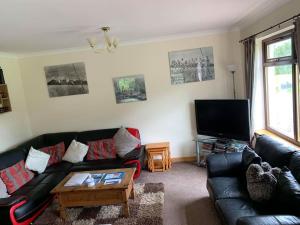a living room with a black leather couch and a tv at Snowberry Cottage No 2 in Onich
