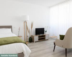 een slaapkamer met een bed, een stoel en een televisie bij TRIADE Apartamentos in Aveiro