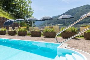 a swimming pool with umbrellas and chairs with mountains in the background at Hotel Alle Piramidi in Segonzano