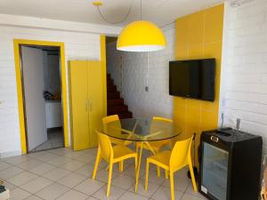 a dining room with a glass table and yellow chairs at Paraíso Pé na Areia em Maragogi in Maragogi