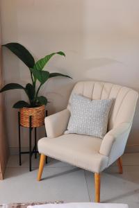 a white chair in a living room with a plant at Square Connexions Guest House in Gaborone