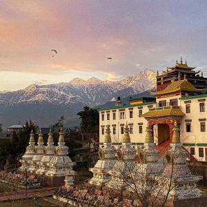 a large white building with mountains in the background at Chokling ArtHouse - The Treasure of Himalayas in Bīr