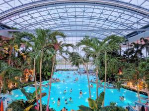 une grande piscine intérieure avec des palmiers et des personnes y séjournant dans l'établissement HOLT - Welcome to the Jungle, à Bucarest