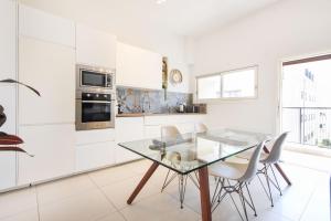 a white kitchen with a glass table and chairs at Lily of the Valley by HolyGuest in Tel Aviv