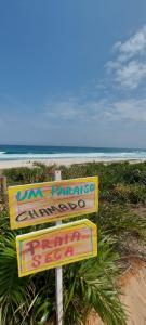 a sign at the beach with the ocean in the background at Aluguel Casa em Praia Seca in Rio de Janeiro
