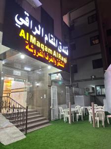 een restaurant met witte tafels en stoelen en een bord bij فندق المقام الراقي للشقق والغرف المفروشة in Mekka
