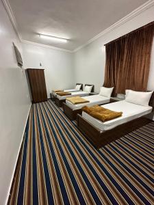 a hotel room with three beds and a striped carpet at فندق المقام الراقي للشقق والغرف المفروشة in Makkah