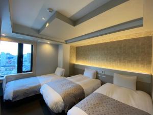 東京にあるアパホテル〈京急蒲田駅前〉のベッド3台と窓が備わるホテルルームです。
