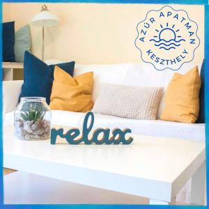 a white couch with pillows and a sign that reads relax at Azúr Apartman Keszthely in Keszthely