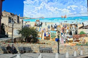 une fresque murale sur un mur avec des personnes assises sur des bancs dans l'établissement Casa Vacanza Il Murales, à Loceri
