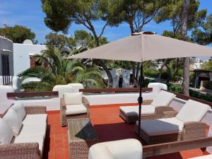 Un patio con sillas blancas y una sombrilla. en Apartamentos Osa Menor, en Cala d´Or