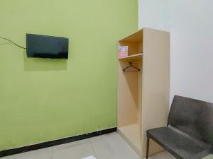 a room with a chair and a television on a wall at Reddoorz at Cempaka Guesthouse Tarakan in Sibengkok