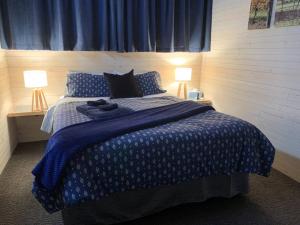 een slaapkamer met een blauw en wit bed met 2 lampen bij The Shedhouse at Milbrodale Farm in Bulga