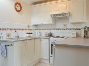 una cocina blanca con armarios blancos y fregadero en The Annexe, en Newchurch