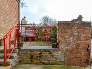 uma parede de tijolos com um portão vermelho e um banco em The Annexe em Newchurch