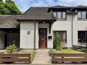 a white house with a brown door and a yard at Ceol Na Mara in Dornoch