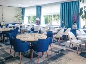 a restaurant with white tables and blue chairs at Hôtel Mercure Mâcon Bord de Saône in Mâcon