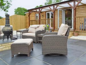 a patio with wicker chairs and a wood stove at Cedar Lodge in Herstmonceux