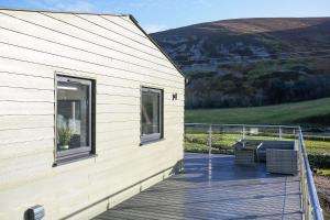 a wooden deck next to a building with a table at Castlehill cabin with a hot tub in Peebles