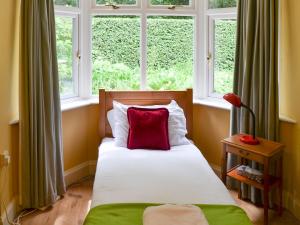a bed with a red pillow in a room with windows at The Anchorage in Wroxham