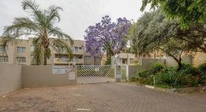 a gate with trees and flowers in front of a building at RAD STAYS - 26 Madison Palms East 112 North Road Sandown in Johannesburg