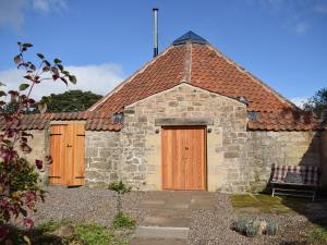 a small stone building with wooden doors and a roof at The Roondie in Ladybank