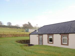 a small white house with a grassy yard at Liftingstane Cottage in Closeburn