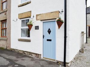 una casa blanca con una puerta azul y dos plantas en Parsley Cottage, en Tideswell