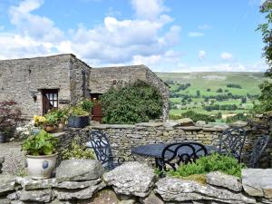 un mur en pierre avec une table et des chaises devant un bâtiment dans l'établissement The Old Goat House, à Aysgarth