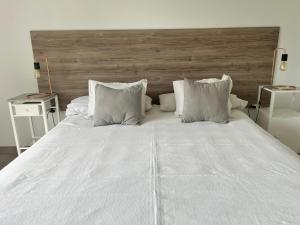 1 cama blanca grande con almohadas blancas y cabecero de madera en Pergolas Guest House - Pileta, Vinos y Montaña en Vista Flores