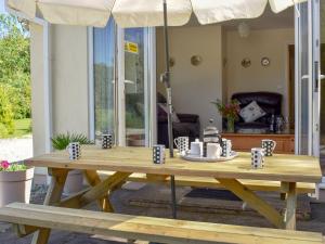 a wooden picnic table with an umbrella on a patio at Green Valley Retreat in Holsworthy