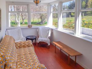 a living room with a couch and two chairs and windows at Ivy Cottage in Mountblairy