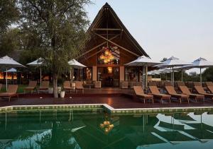 a pool with chairs and umbrellas in front of a building at Letamo at Qwabi Private Game Reserve by NEWMARK in Bela-Bela