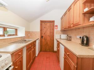 a kitchen with wooden cabinets and a red tile floor at Larch Bed Cottage in Worcester